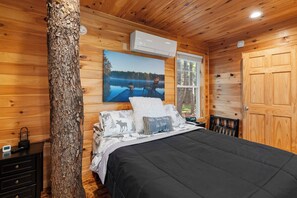 Une chambre dans une cabane en bois, avec un lit, une table de chevet, une fenêtre et une porte.