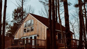 Una baita di legno con un balcone, immersa tra alberi alti.