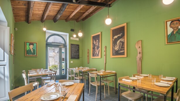 A restaurant with green walls, wooden tables, and chairs. There are framed artworks on the walls and a welcome sign above the door. - Locanda LoSteri (Ragusa)