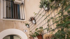 A building with a metal grid wall, potted plants, and a door. - Locanda LoSteri (Ragusa)