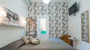 A bedroom with a bed, pillows, a wardrobe, a TV, and a door leading to a bathroom. - Locanda LoSteri (Ragusa)