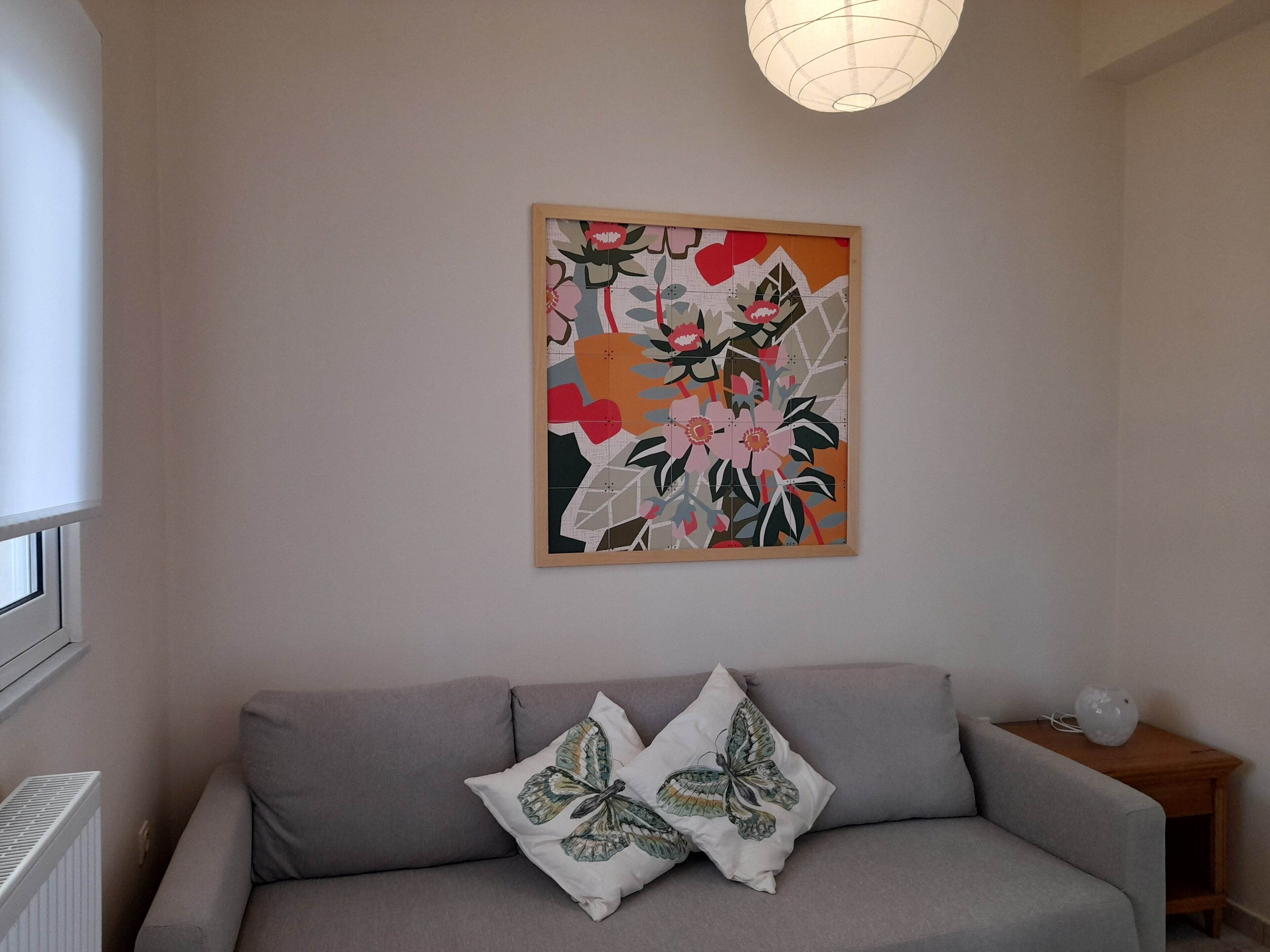 A living room with a grey sofa, two butterfly pillows, and a colorful abstract painting on the wall.