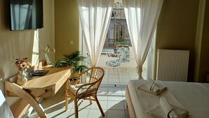 A bedroom with a bed, a desk, a chair, a TV, and a balcony with a table and chairs. - ChaniaStay Central Apartments (Chania)