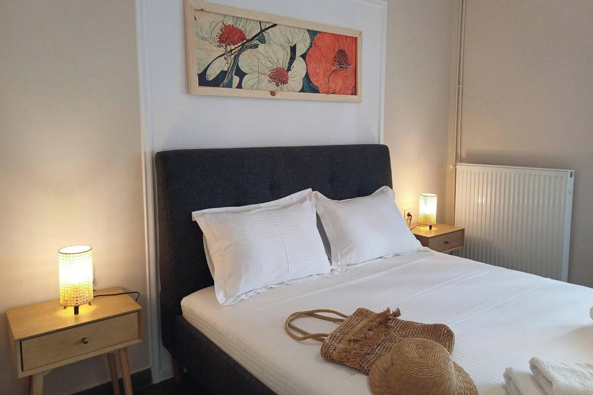 A neatly made bed with white linens, a dark headboard, and a wall-mounted artwork above it.