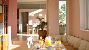 A dining area with a table set for breakfast, including orange juice and a pitcher of orange juice, a potted plant, and a view of the outdoors. - ChaniaStay Central Apartments (Chania)
