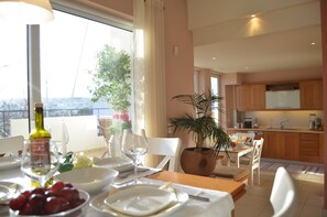 A dining area with a table set for two, a potted plant, and a view of the cityscape through large windows.