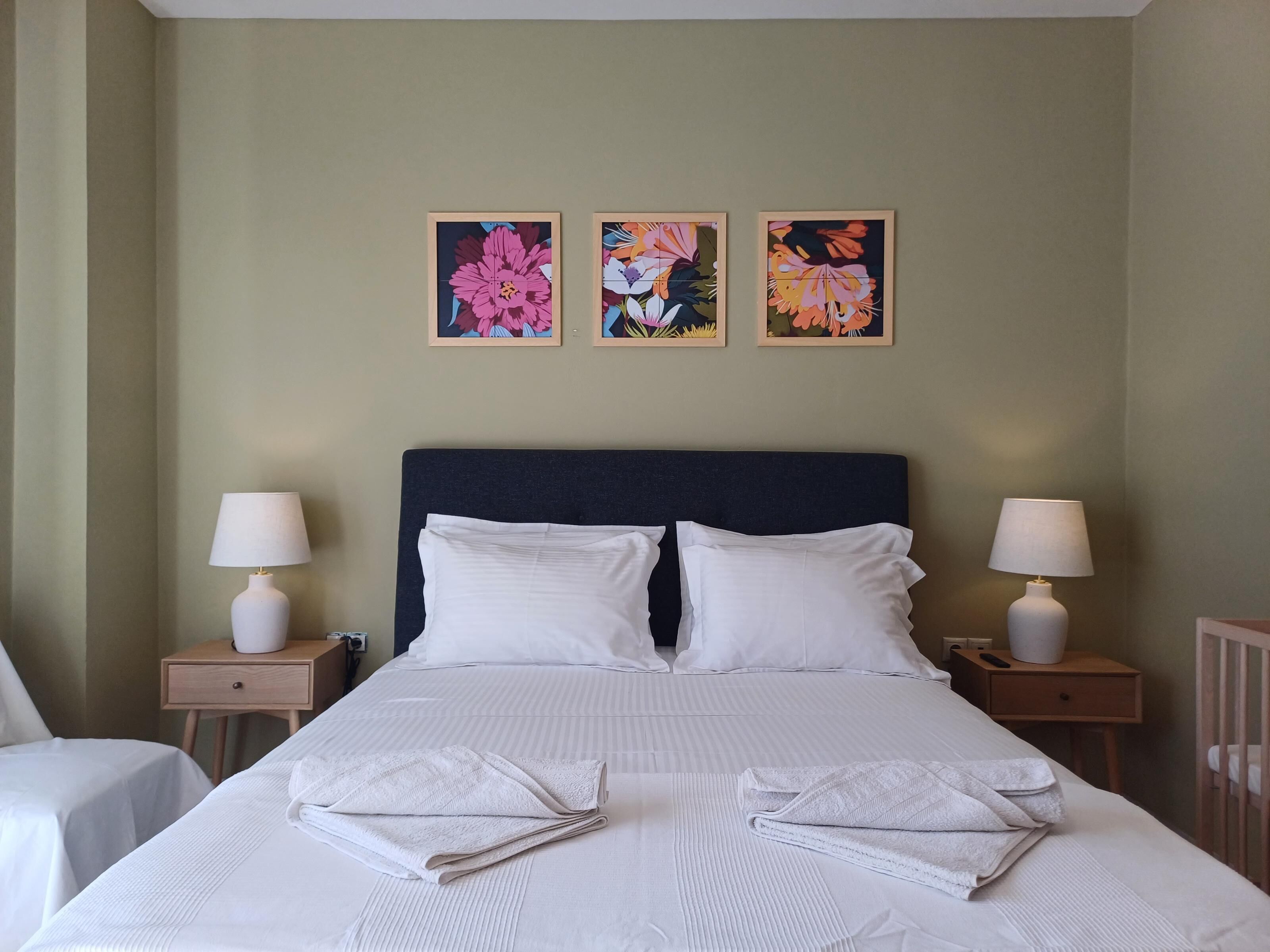 A hotel room with a large bed, two bedside tables with lamps, and three framed floral paintings on the wall.