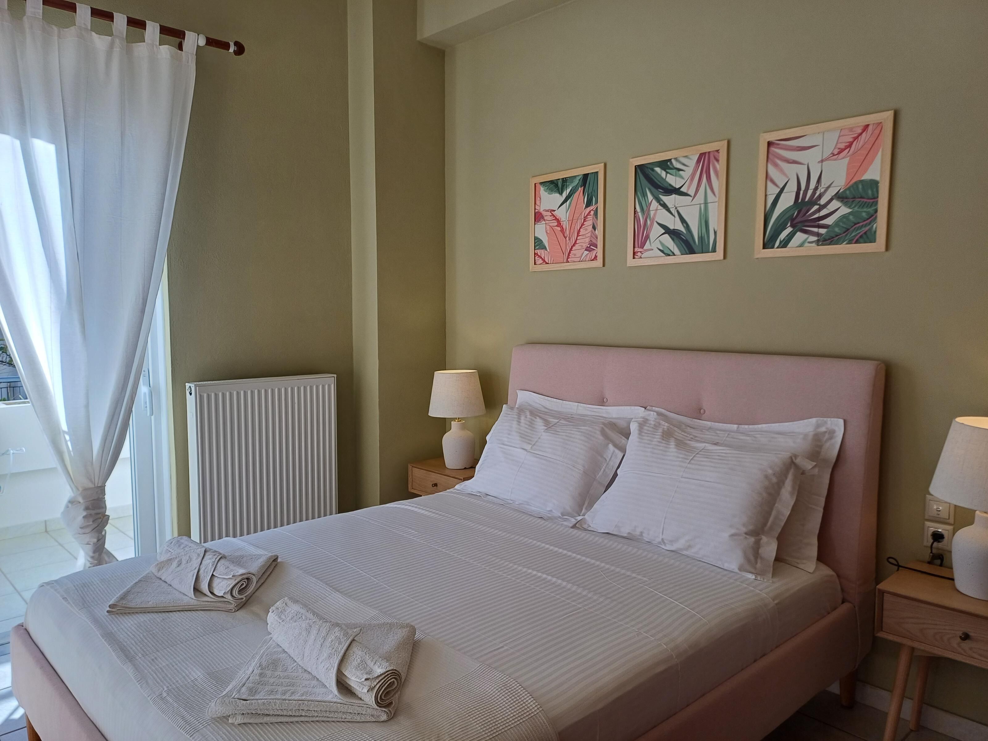 A neatly made bed with white linens and pillows, a bedside table with a lamp, and two framed botanical prints on the wall.