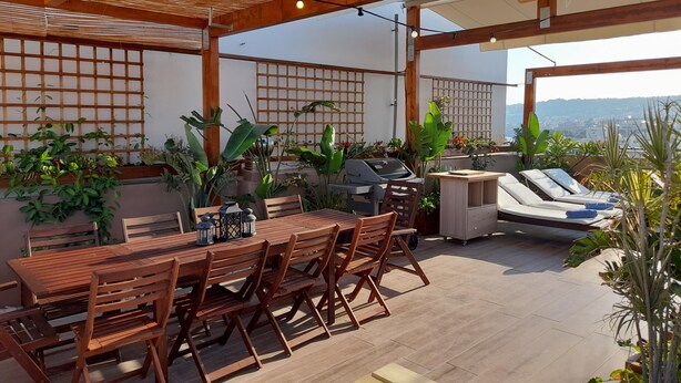 An outdoor patio with a wooden table and chairs, a grill, and various potted plants. - ChaniaStay Central Apartments (Chania)