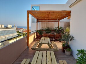 A wooden deck with a table and chairs, surrounded by potted plants, overlooking a cityscape and the sea. - ChaniaStay Central Apartments (Chania)