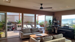 A spacious living room with a sofa, coffee table, and a piano. There is a balcony with plants and a grill. - ChaniaStay Central Apartments (Chania)