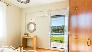Une chambre avec un lit, un bureau en bois, un miroir, une petite plante et une porte-fenêtre coulissante donnant sur un espace piscine.