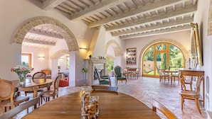 A spacious dining area with wooden tables and chairs, a fireplace, and large windows offering a view of the outdoors. - Le Buche Wine Resort Villa (Sarteano)