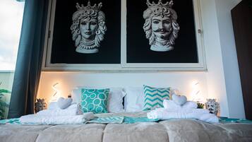 A neatly made bed with white and teal pillows, a decorative headboard, and a framed artwork above.