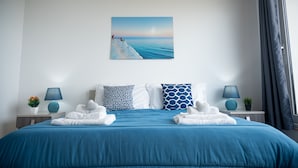Un lit bien fait, recouvert d’une couvre-lit bleue, avec deux coussins à motifs et deux lampes sur les tables de chevet.