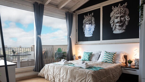 Une chambre dotée d’un grand lit, d’un balcon avec vue et de deux œuvres d’art accrochées au mur.