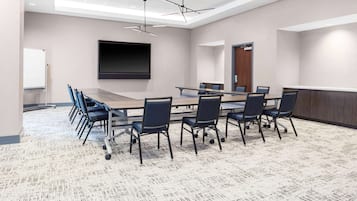 Un salón de conferencias con una larga mesa, sillas, una pantalla de proyector y una pizarra.