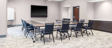 A conference room with a long table, chairs, a projector screen, and a whiteboard.