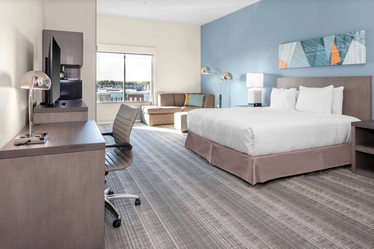 Ein Hotelzimmer mit Bett, Schreibtisch, Stuhl und Blick ins Freie.