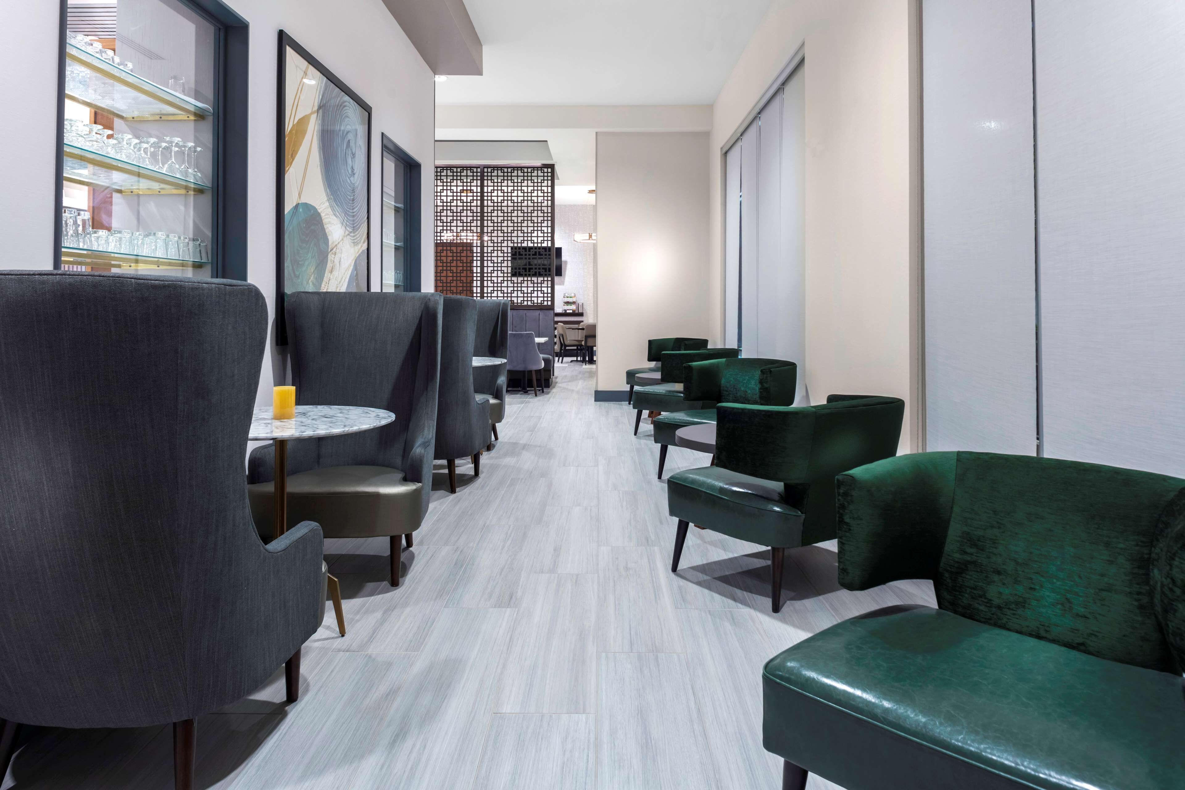 Un área de descanso moderna con asientos tapizados en gris y verde, una vitrina de vidrio y una pantalla decorativa.