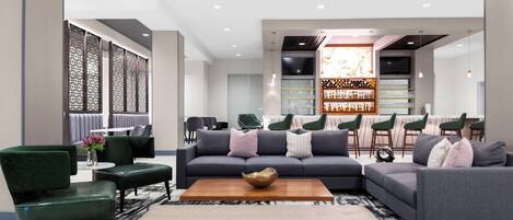 A modern lounge area with sofas, chairs, a coffee table, and a bar area with shelves of bottles and glasses.