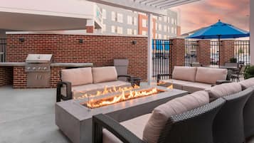 An outdoor patio with a fire feature, seating, and a grill.