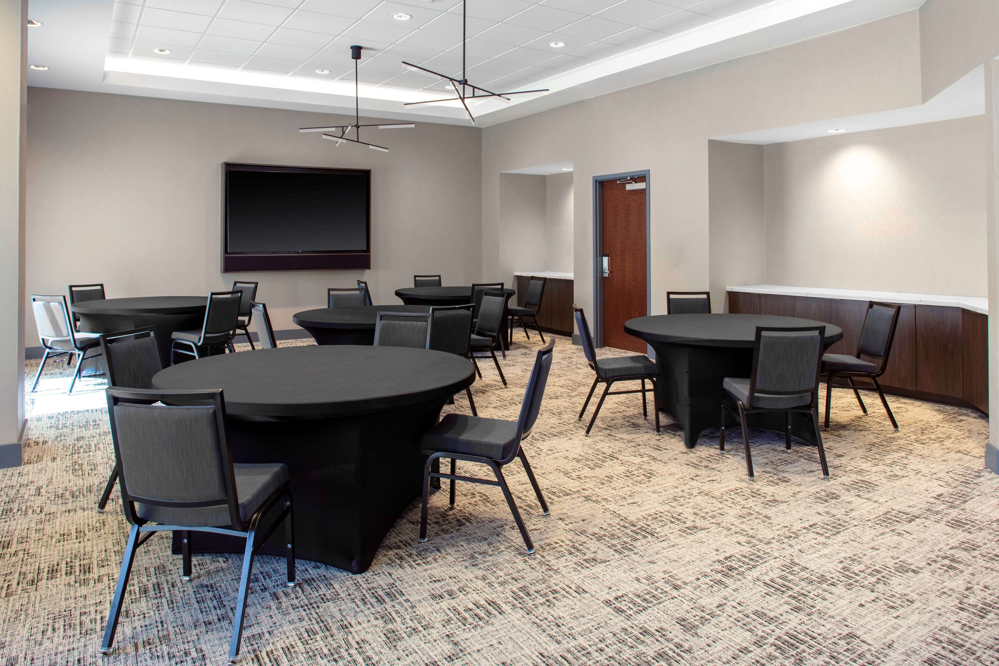 Une salle de conférence dotée de plusieurs tables et chaises, d’un grand écran et d’un sol recouvert de moquette.