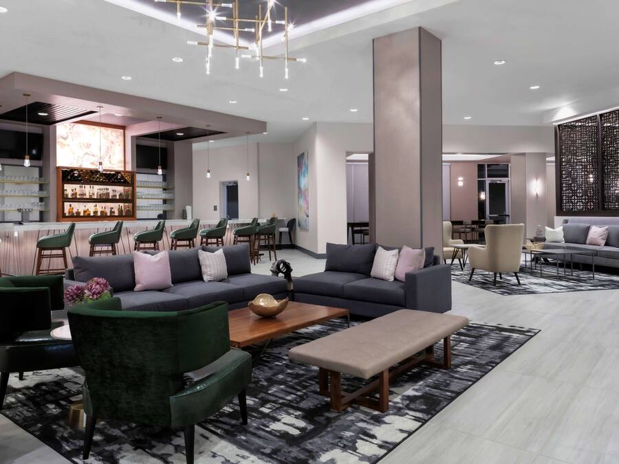 Un moderno vestíbulo de hotel con zona de bar, arreglos de asientos y un gran muro decorativo.