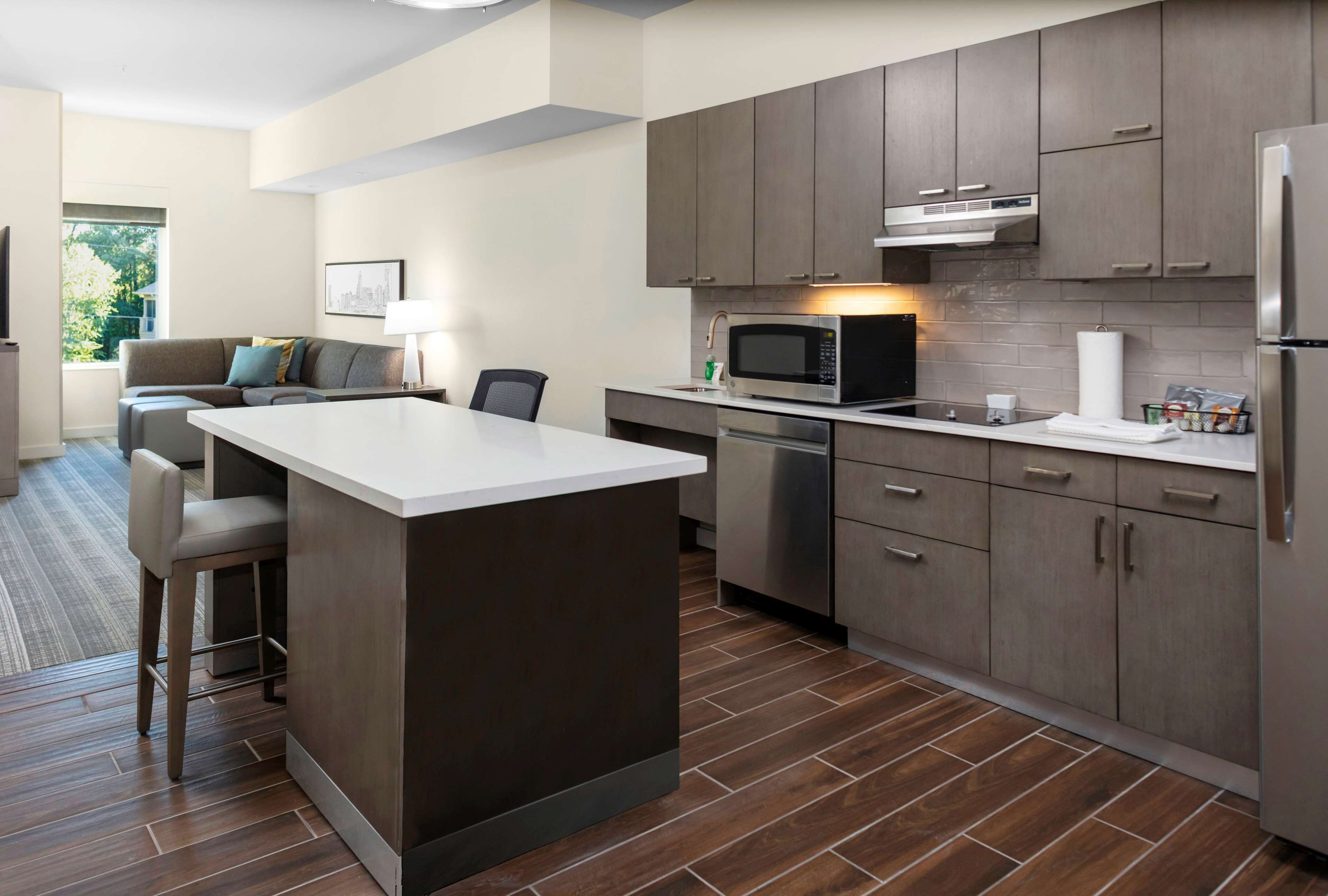 Una cocina moderna con armarios de madera oscura, una isla central, electrodomésticos de acero inoxidable y vista al área de estar.