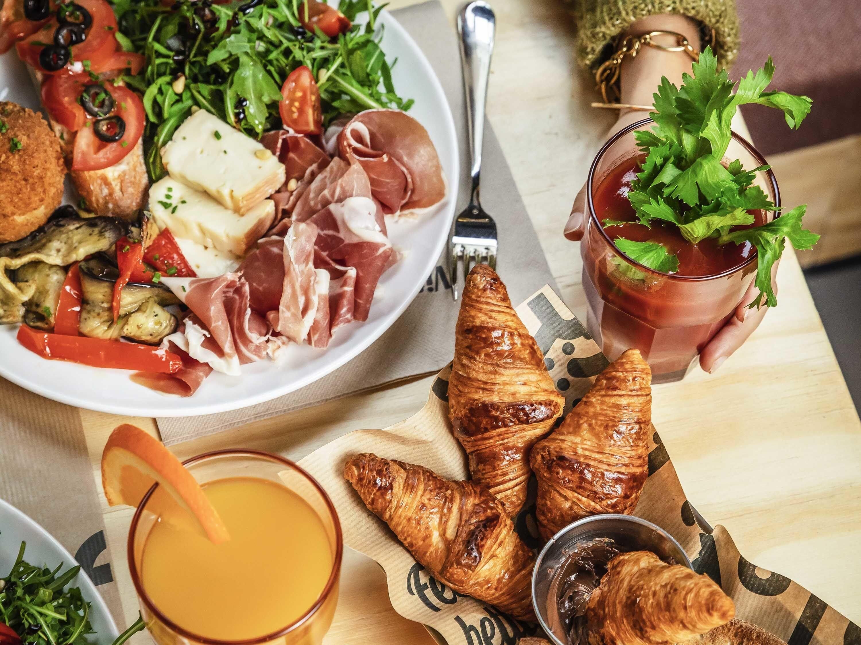 Een ontbijttafel met croissants, een bord eten met groenten en vlees, een glas jus d'orange en een kopje thee met garnering.