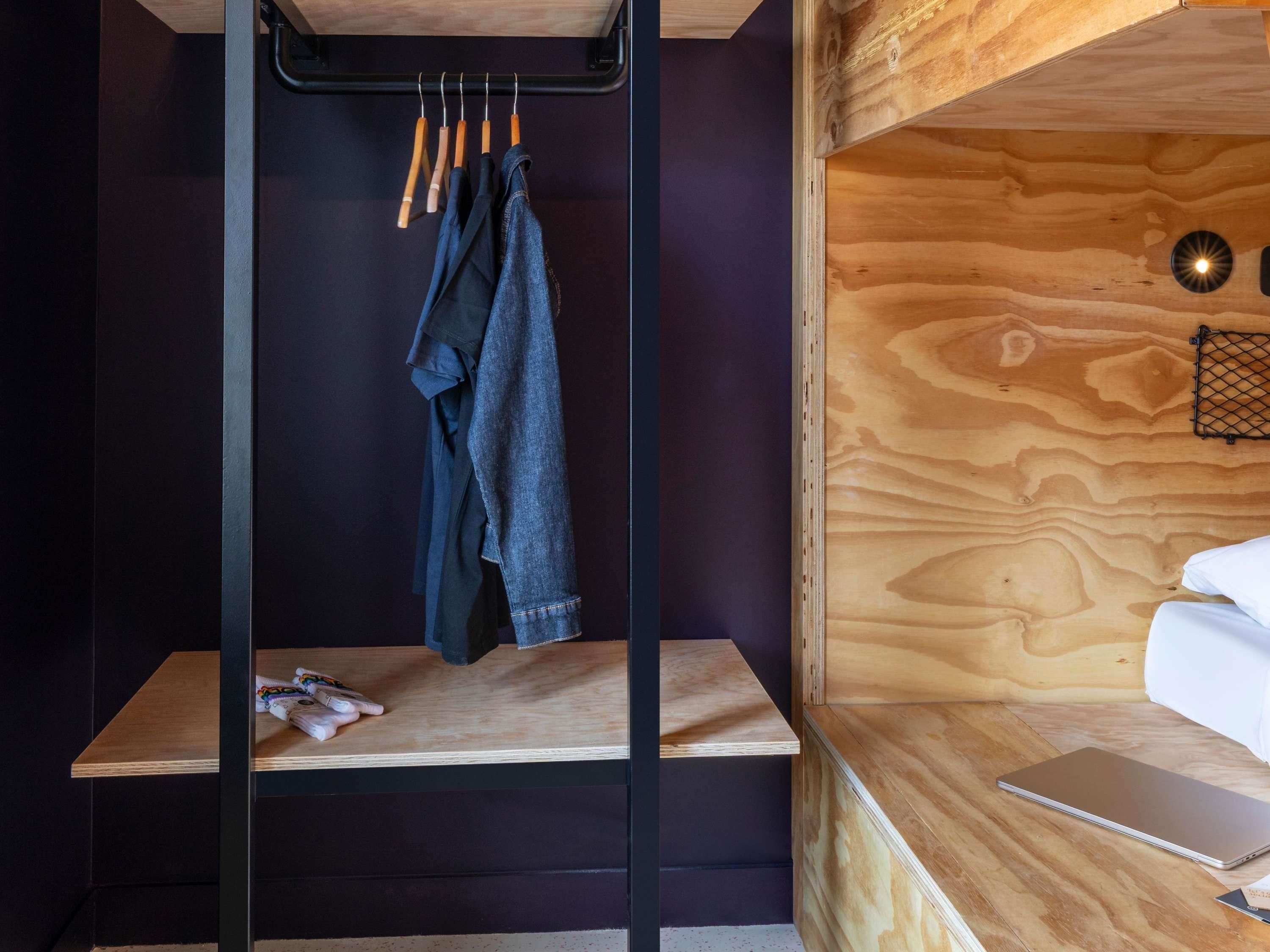 Ein Etagenbett mit Holzkopfende, ein Regal mit Büchern und eine Kleiderstange mit Kleidung.