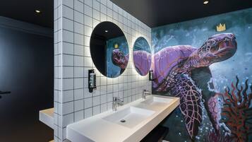 Een moderne badkamer met een grote wastafel, twee spiegels en een muurschildering van een zeeschildpad.