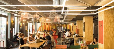 A spacious indoor dining area with high ceilings, exposed ductwork, and modern pendant lighting.