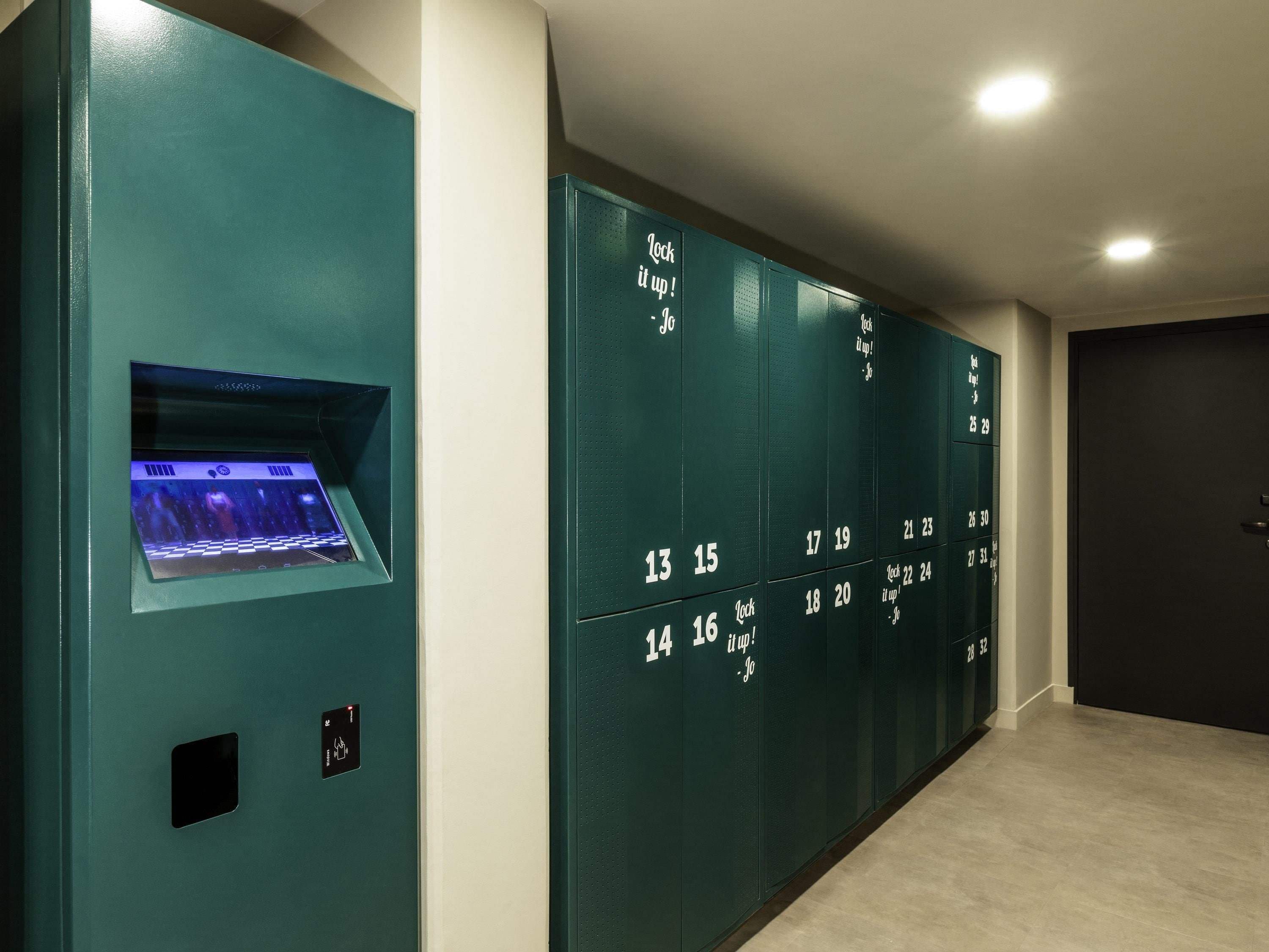 Una hilera de taquillas turquesa con números, una pantalla digital y una puerta a la derecha.
