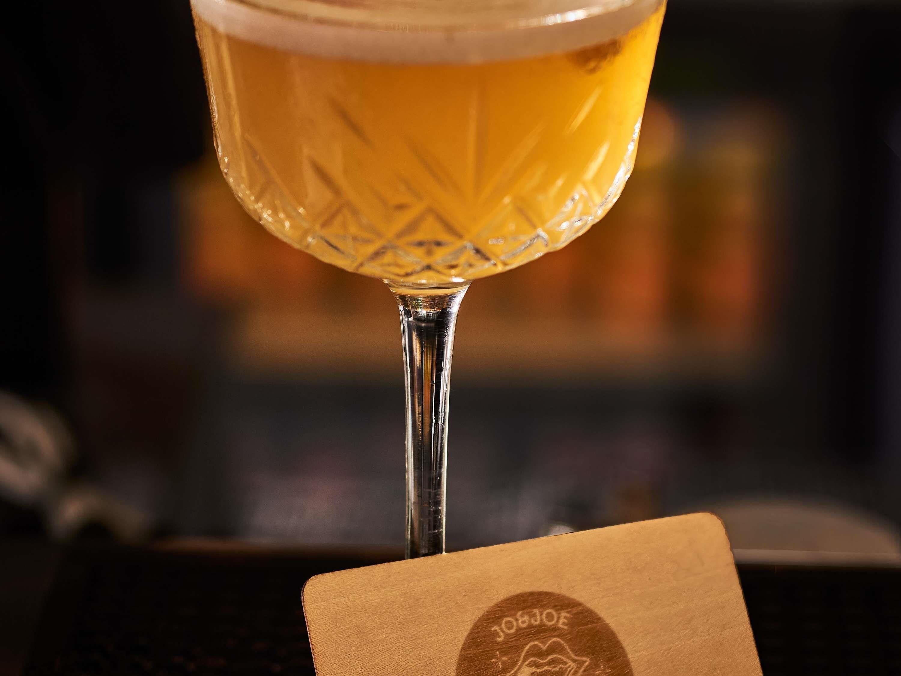 Un verre de bière posé sur un dessous de verre orné d’un logo, le tout sur un fond flou.