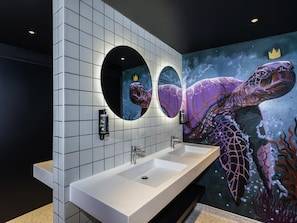 Une salle de bain avec deux lavabos, un grand miroir et une fresque représentant une tortue de mer.