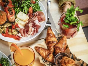 A breakfast setting with croissants, a plate of food including vegetables and meats, a glass of orange juice, and a cup of tea with a garnish. - Jo&Joe Paris Nation - Hostel (Paris)