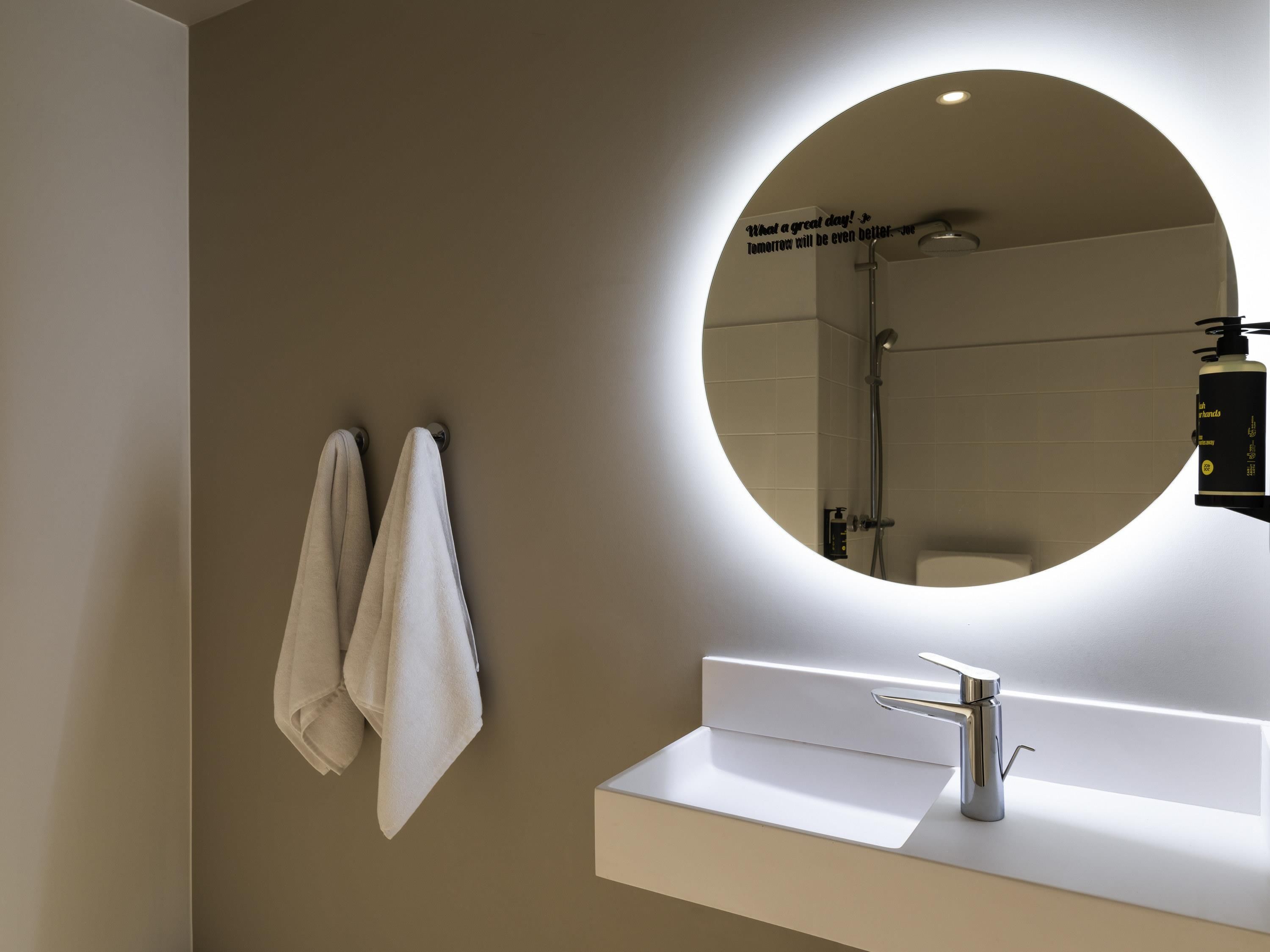 A modern bathroom with a round mirror, a white sink, and two towels hanging on the wall.