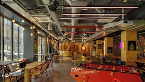 A modern interior with tables, chairs, a foosball table, and large windows. - Jo&Joe Paris Nation - Hostel (Paris)