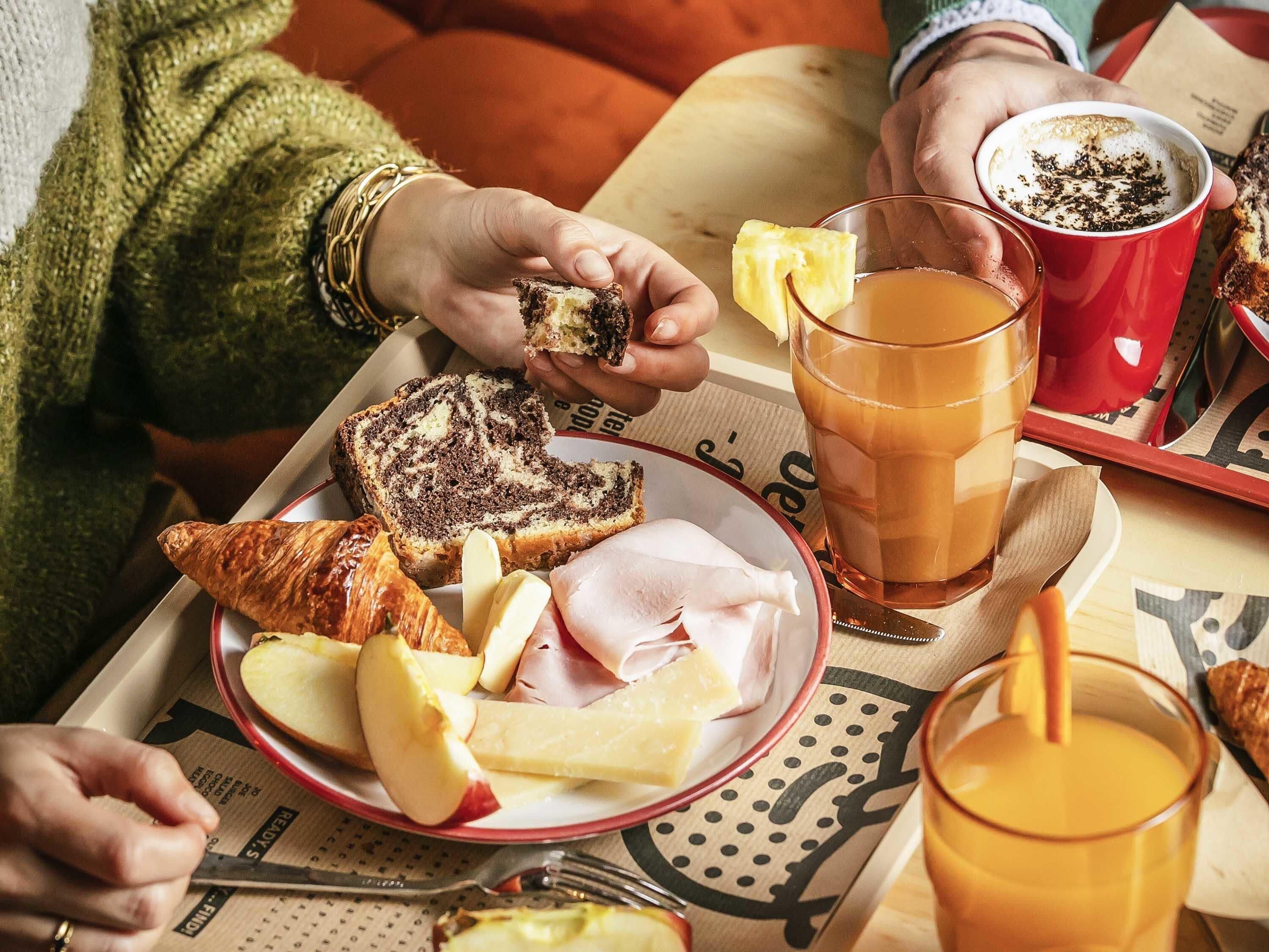 A tray with food items including bread, ham, cheese, and apples, along with a glass of orange juice and a cup of coffee.