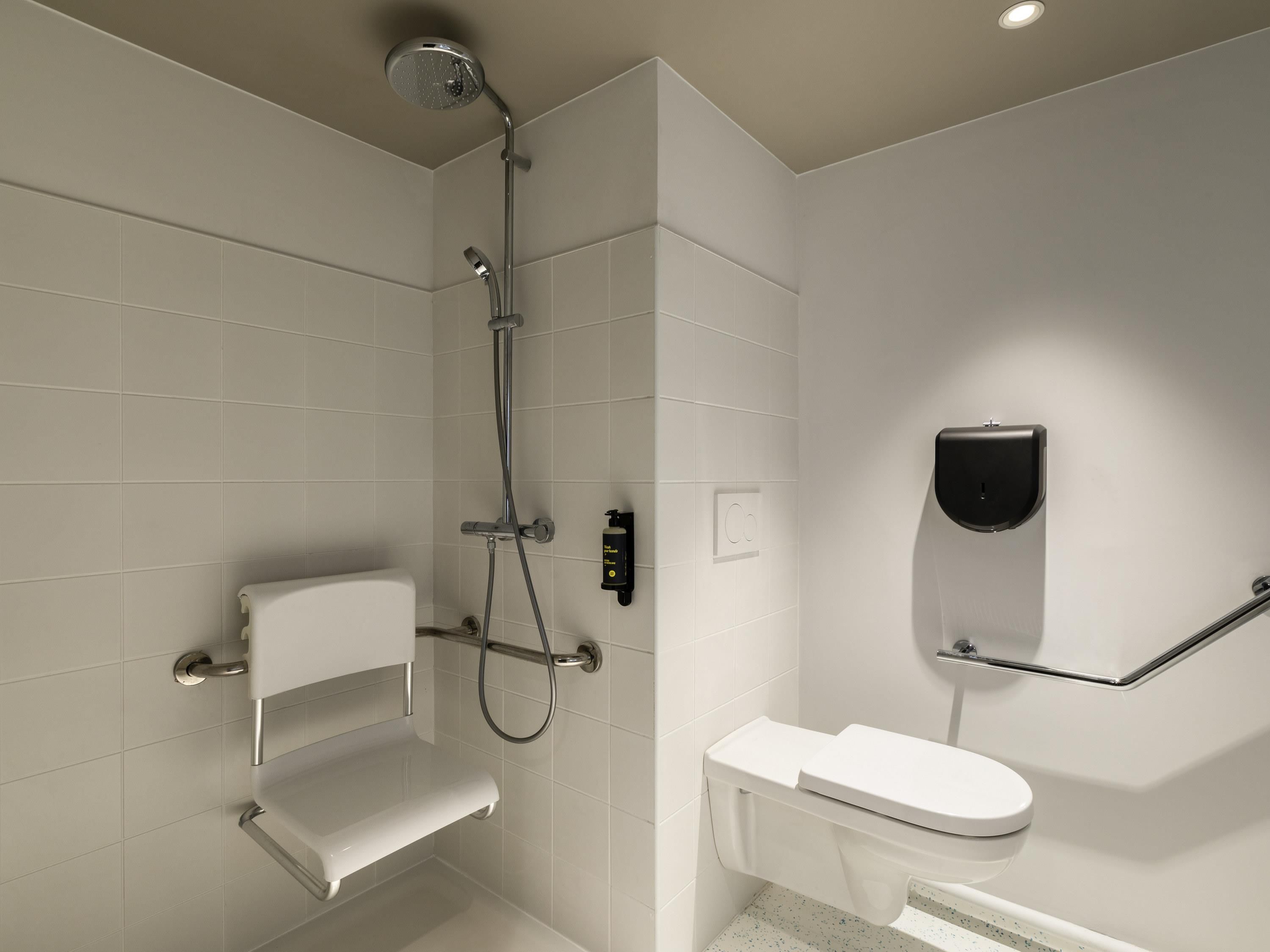 Un baño moderno con ducha, inodoro y dispensador de gel antibacterial.