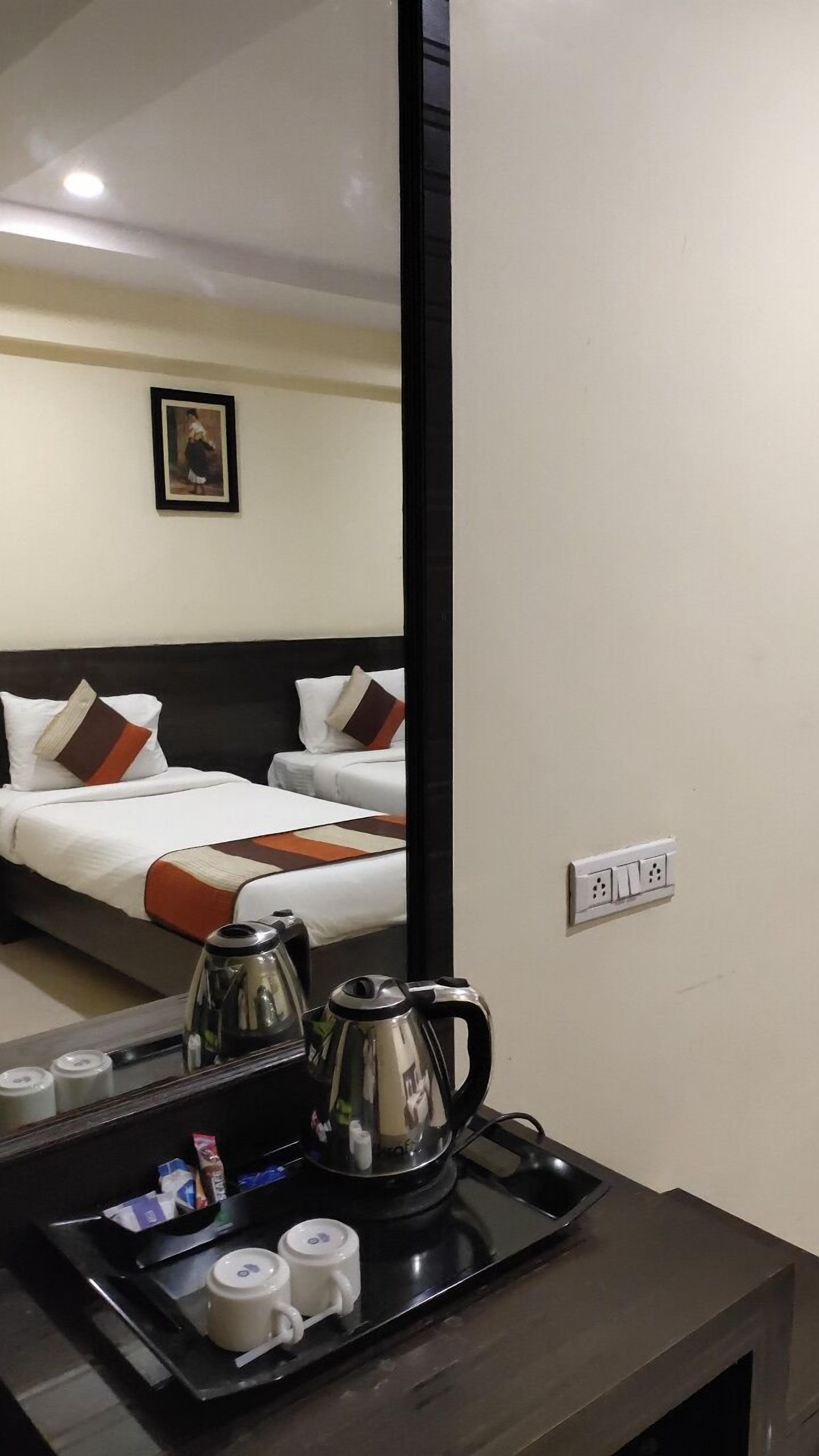 Une chambre d’hôtel comprenant un lit, une table de chevet avec une bouilloire et des tasses, et une prise de courant fixée au mur.