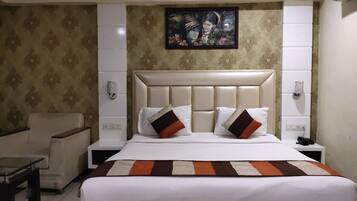 Habitación de hotel con una cama grande, una mesita de noche, una silla y un cuadro en la pared.