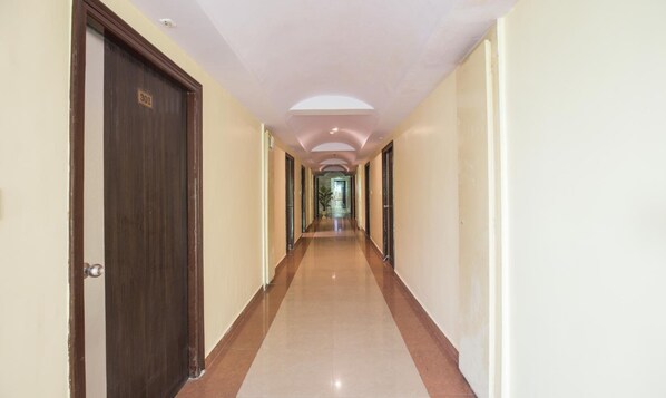 A long, narrow hallway with a tiled floor, doors on both sides, and a ceiling with recessed lighting. - Hotel City Square by KeyMagics (Jodhpur)