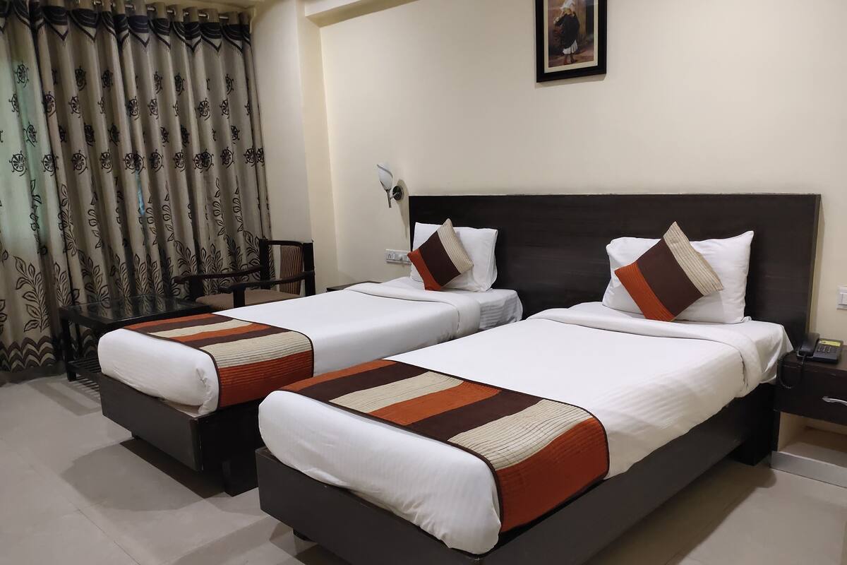 A hotel room with two beds, a desk, a chair, and a large window with curtains.