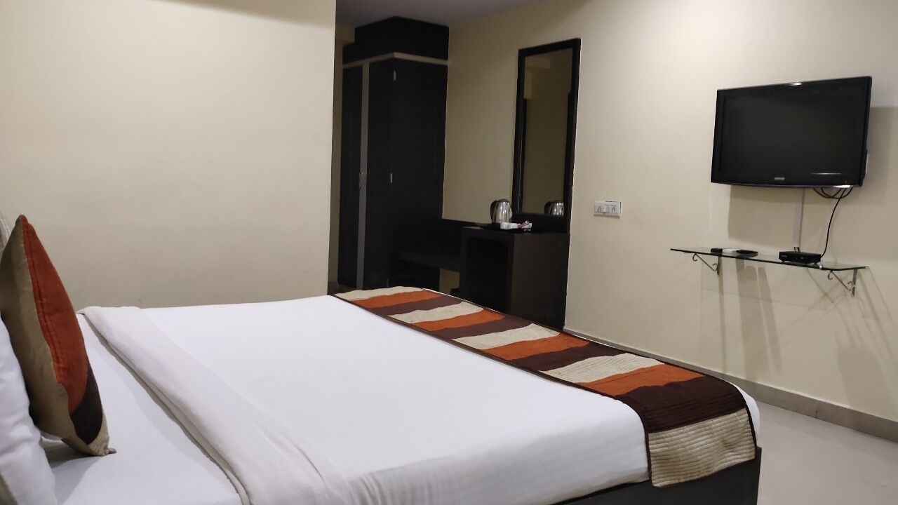 Habitación de hotel con cama, televisión montada en la pared, espejo y una mesita con control remoto.