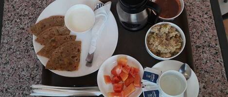 A tray with food items including flatbreads, a bowl of fruit, a cup of tea, and a bowl of soup.