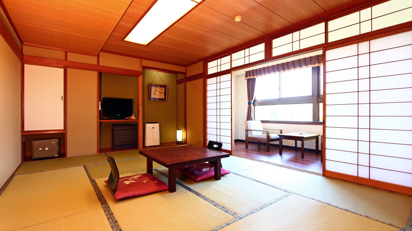 Una habitación japonesa tradicional con suelo de tatami, una mesa baja, un televisor y puertas correderas.