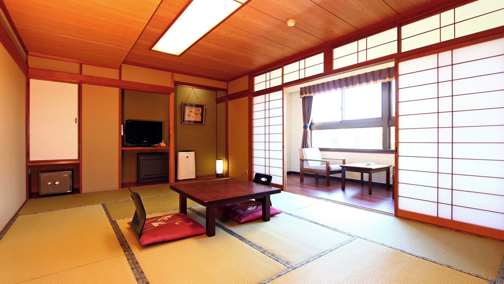 Una habitación japonesa tradicional con suelo de tatami, una mesa baja, un televisor y puertas correderas.