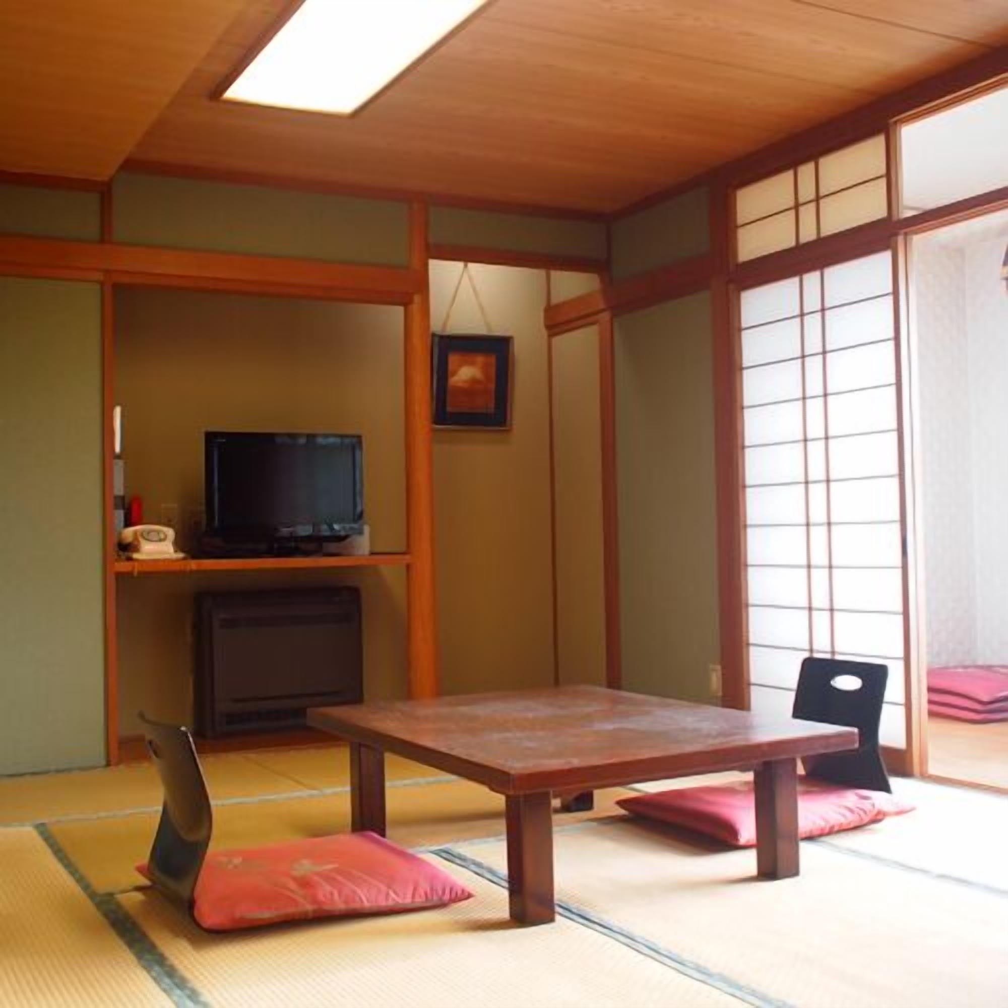 Una habitación japonesa tradicional con suelo de tatami, una mesa baja, un televisor y puertas correderas.